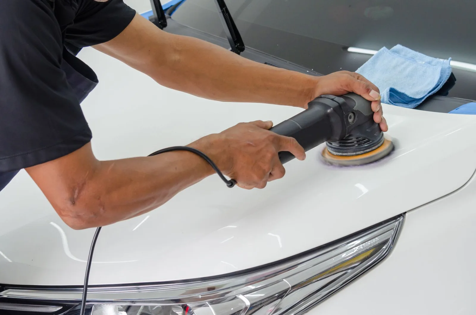 A detailer polishing a car body panel in a workshop
